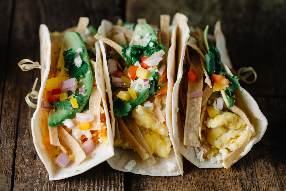 Breakfast tacos with scrambled eggs, avocado, fresh peppers and onions on rustic surface. 