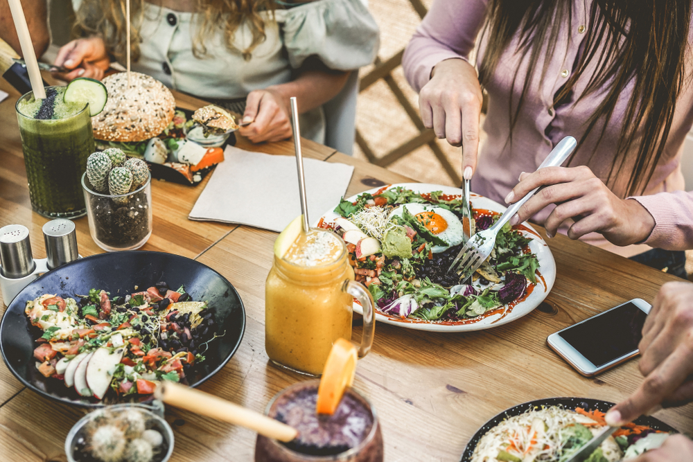 Hands view of young people eating brunch and drinking smoothies bowl with ecological straws in plastic free restaurant. 