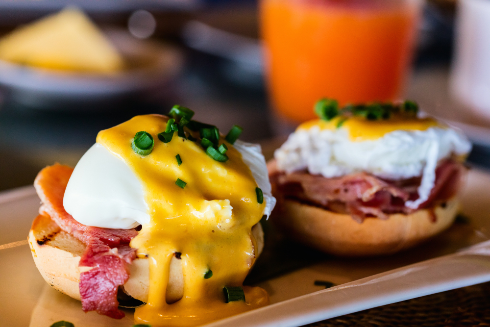 A close up of two eggs benedict on a roll with meat and chives on top