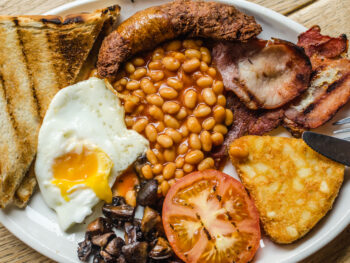 A large plate with eggs, toast, beans, sausage, ham, tomatoes, mushrooms, and a hash brown that you can find for breakfast in Dublin