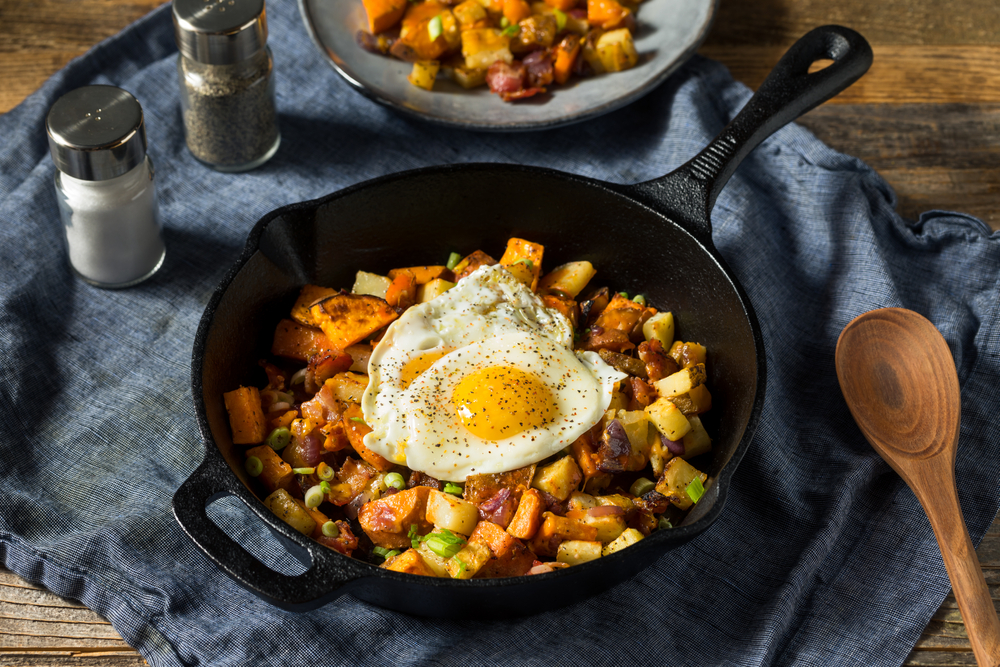 A skillet full of potatoes, bacon, and other foods with a fried egg on top
