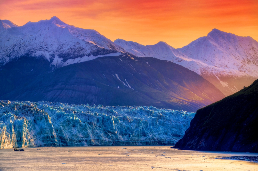 Vivid sunset over mountains, a glacier, and water in Alaska.