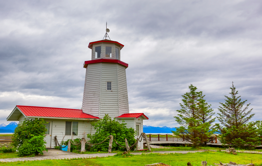 The grey and white Homer Lighthouse with mountains in the far distance across the water.