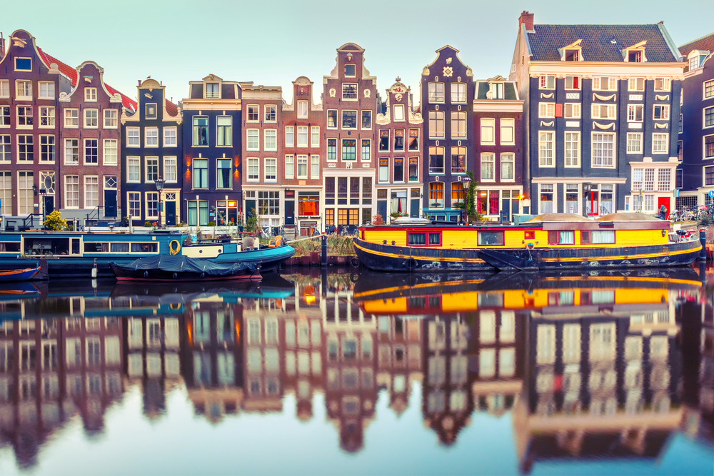 A view of the buildings in Amsterdam along the canal with colorful boats in the canal