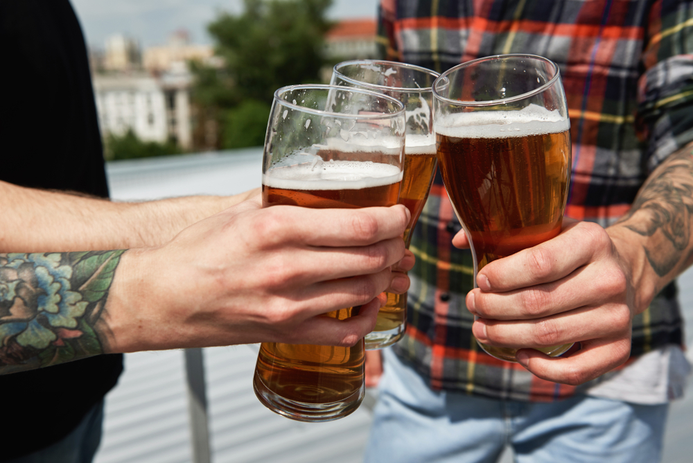 Three people saying cheers with their pint glasses on a rooftop bar. 