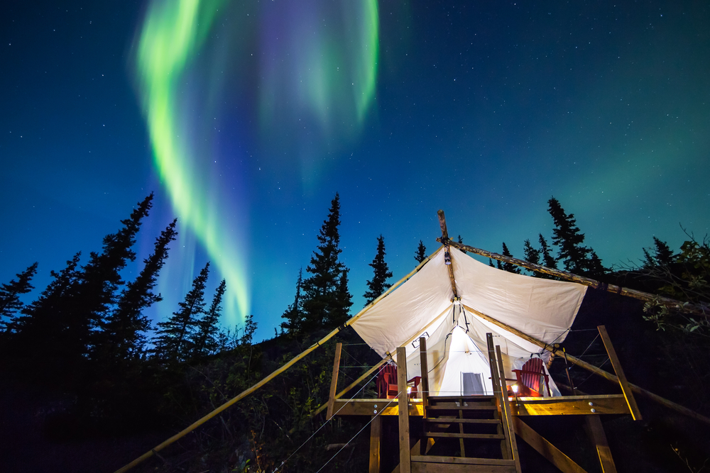 Aurora Borealis glowing green and pink over large canvas luxury camping tent in Alaska