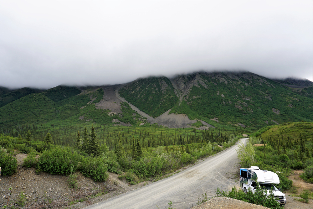 Lone campervan rv on in cloudy weather. There are mountains in the background. 
