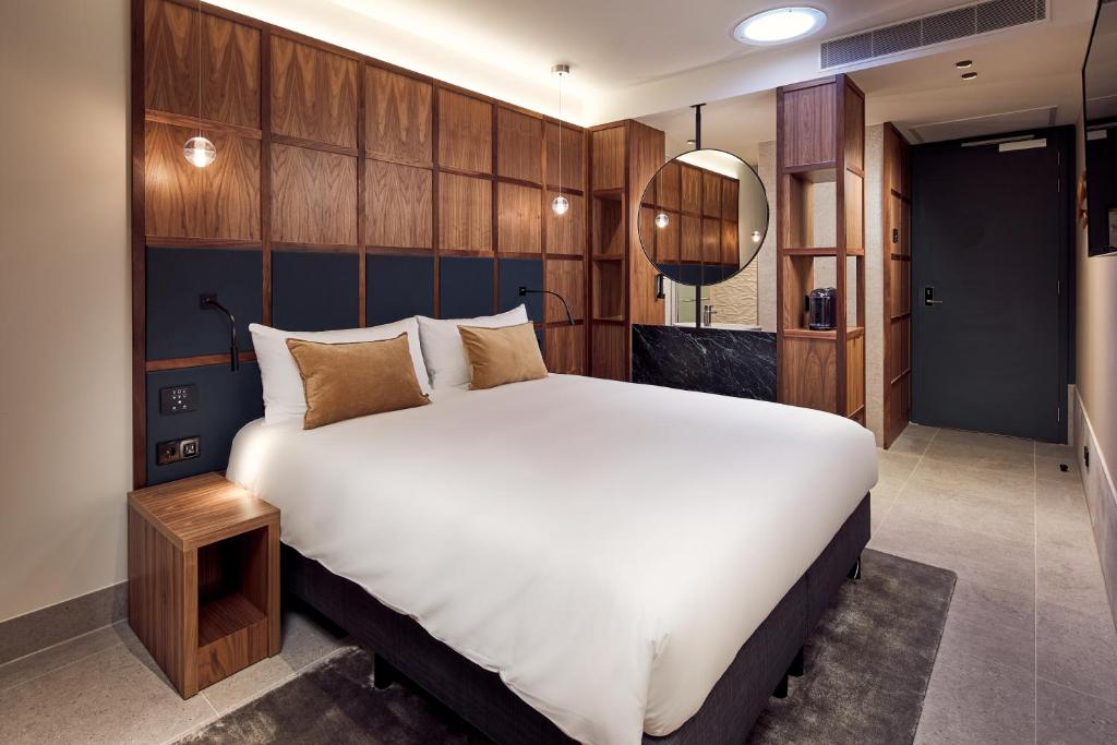 A simply decorated and modern hotel room with wood paneling and a crisp white bedspread. 