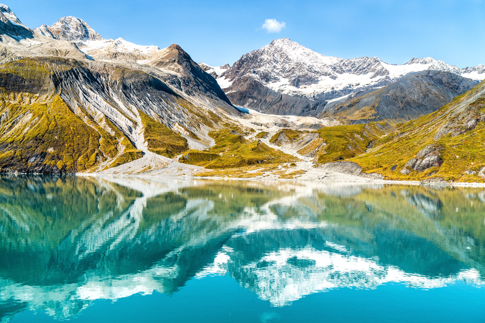 Amazing glacial landscape showing mountain peaks and glaciers on clear blue sky summer day. Mirror reflection of mountains in still glacial waters. The article is about national parks in Alaska.  