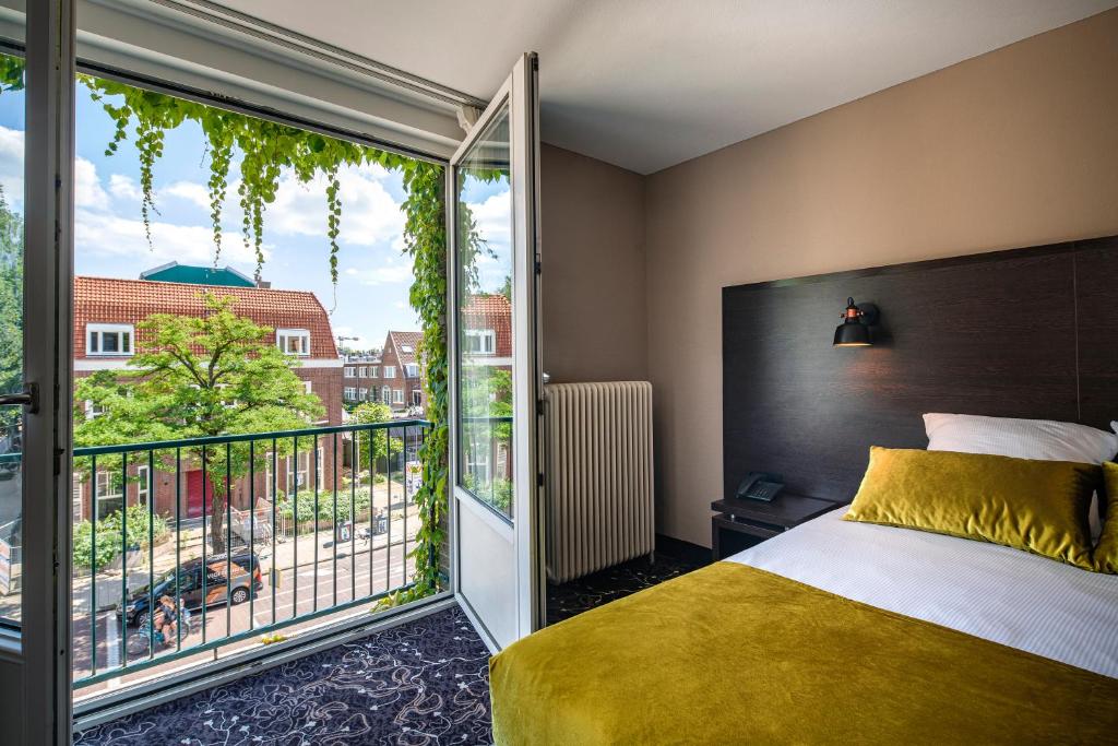 A room in a boutique hotel in Amsterdam that has a gold velvet bed and a door that opens up to a view of the city with foliage around the door