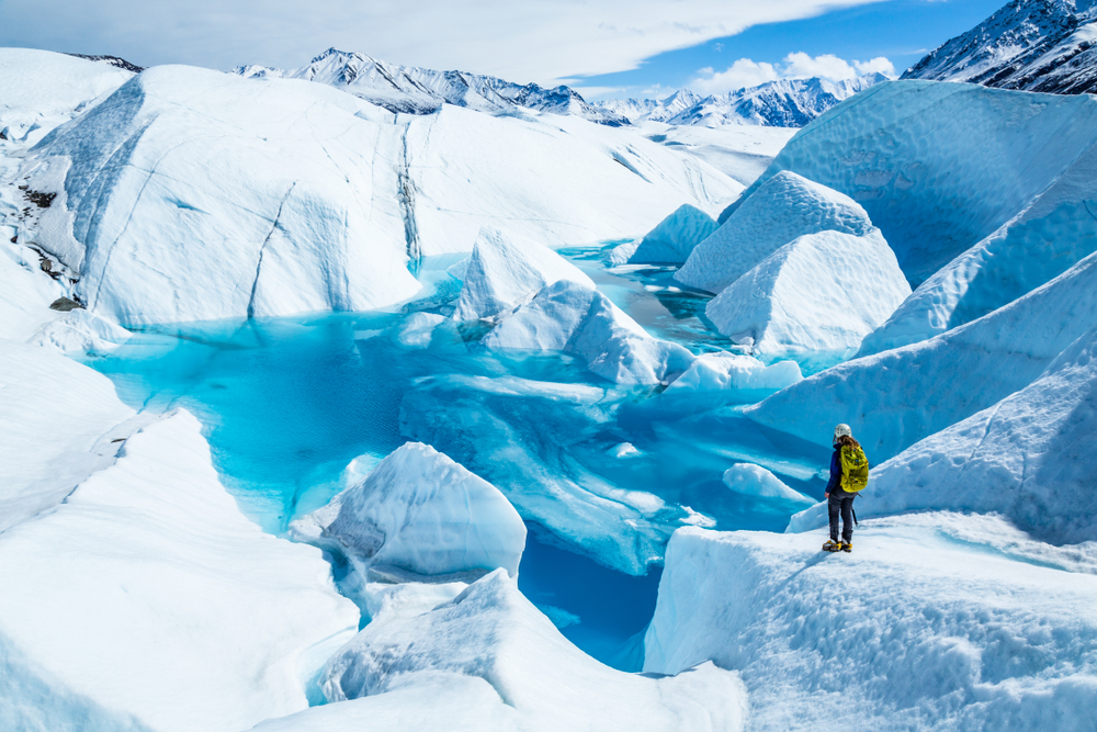 large glacier in Alaska with deep blue ice on a sunny day with female in front of it.