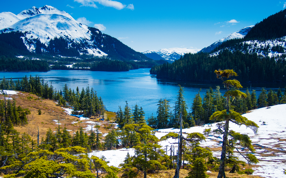 View from above a blue lake surrounded by mountains with snow in Alaska in May.