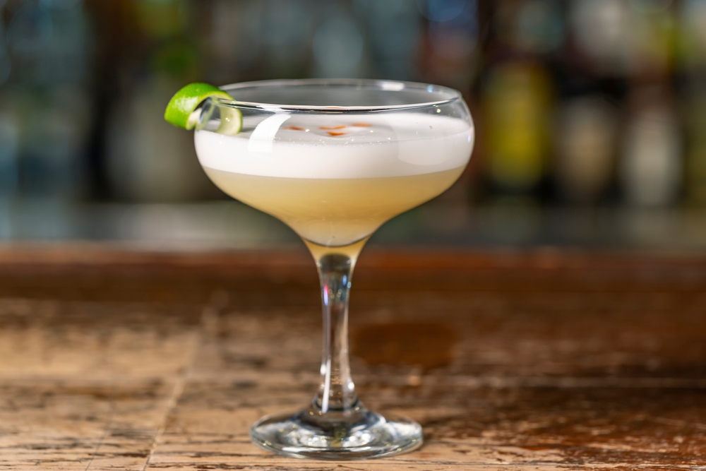 Pisco Sour cocktail on the bar. Blurred background. Peruvian, Mexican, Chilean traditional drink pisco sour liqueur with lime and egg.