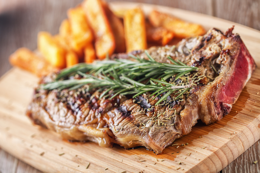 Grilled steak with freid on a wooden plate. There are herbs on the steak. 