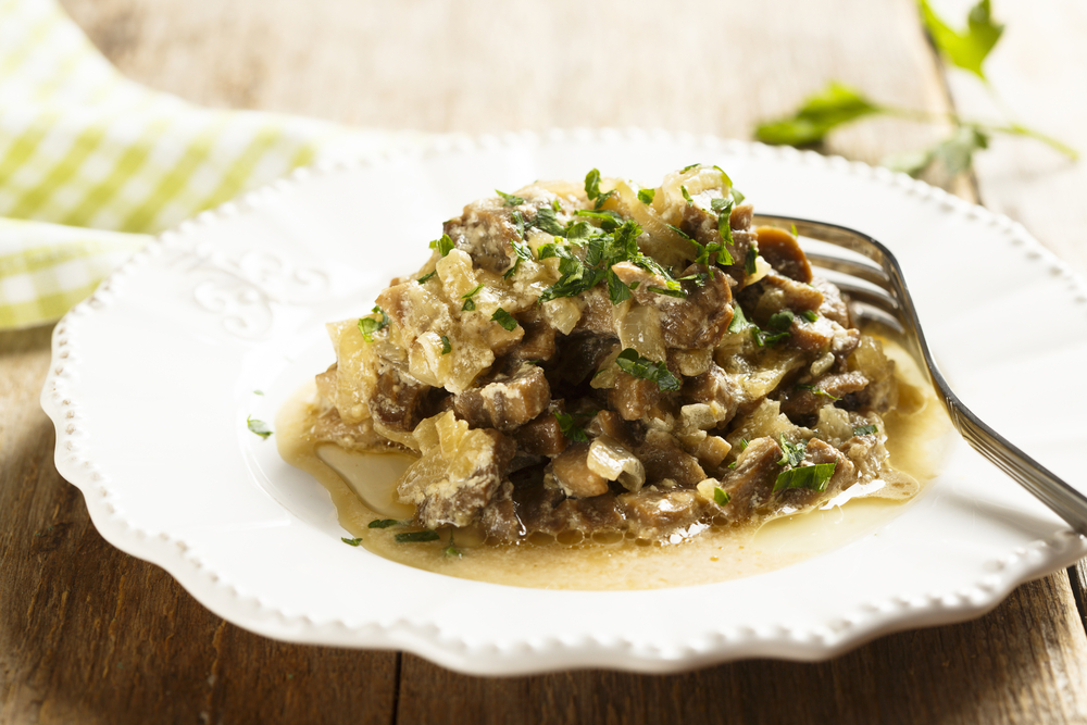 Mushroom ragou with sour cream and parsley on a white plate. There is a fork on a plate  