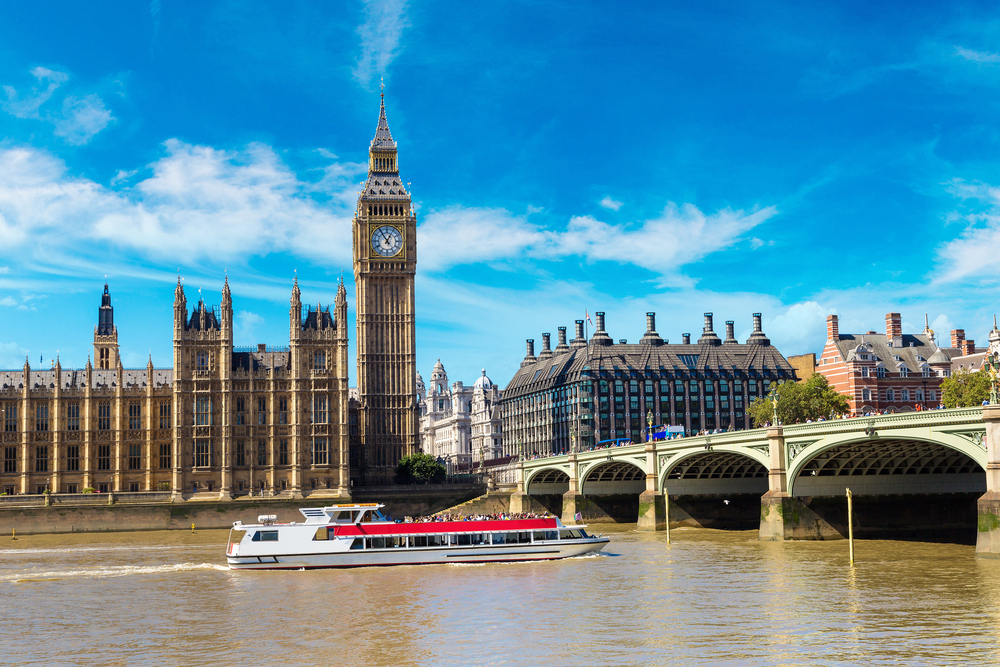 The Big Ben, the Houses of Parliament and Westminster bridge in London in a beautiful summer day. There is a boat crossing under the River Thames. This is one of the things to do with kids in London. 
