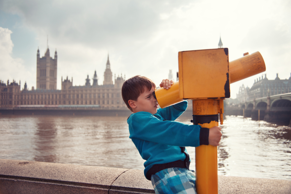 Child looking through coin operated high powered binoculars. View of the Palace of Westminster from the Thames. The article is about London with kids  