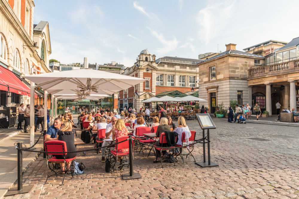A view of Covent Garden showing the plazza and tables and chairs outside.  