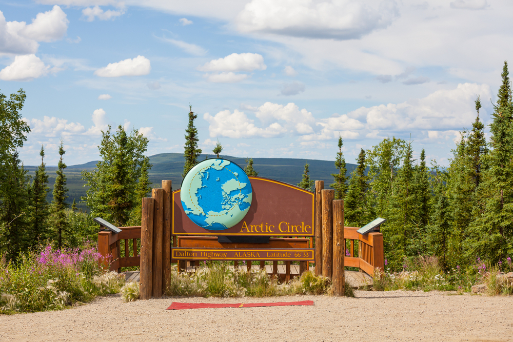 arctic circle board on Alaska with trees and mountaines behind it. 