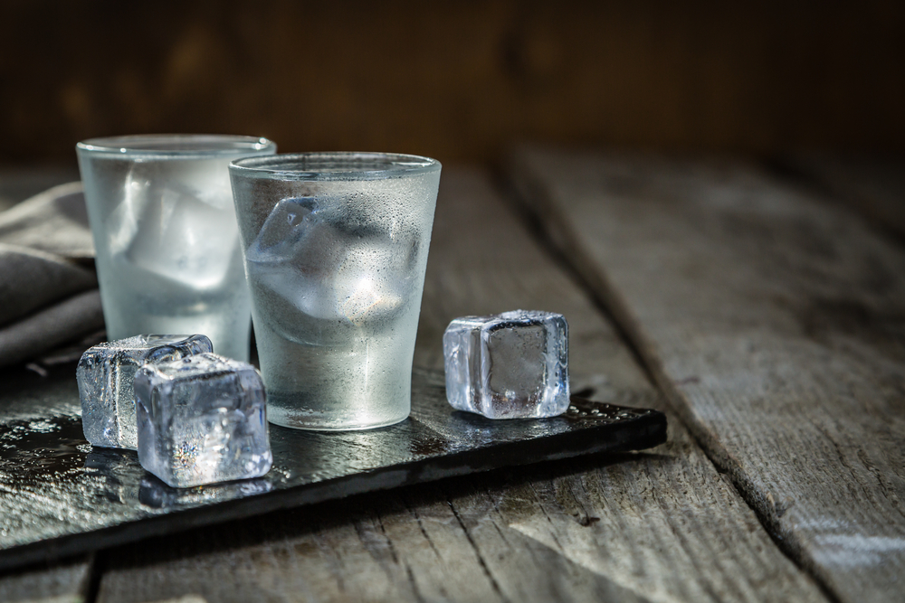 Vodka in shot glasses on rustic wood background with ice by the side. 