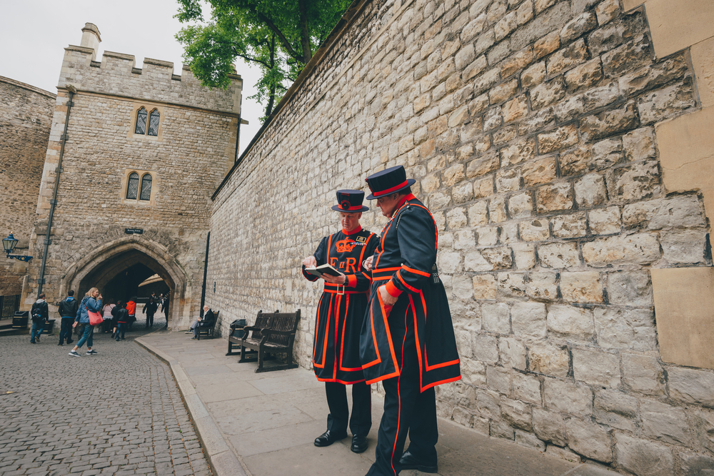Beefeater guards or Yeoman warders at the Tower of London. They are outside the tower looking at a notebook. 