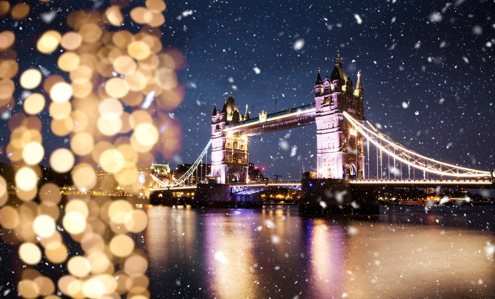Wintery scene on the river Thames. Tower Bridge is lit up as its night and  there are blurred lights in the foreground. 
