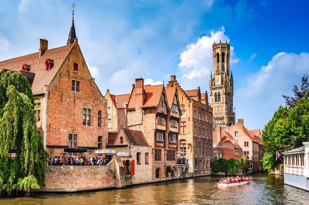 Historic buildings overlooking a canal with a tour boat in Bruges, one of the best day trips from Paris by train.