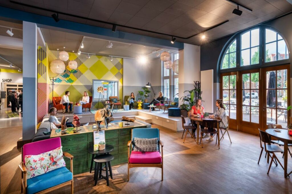 Colorful lounge area at the Stayokay Hostel Amsterdam Oost with people talking and working.