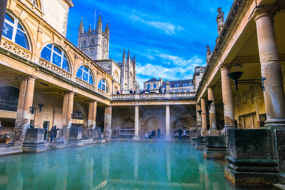 Steaming Roman Baths in winter. There are pillars around the water. 