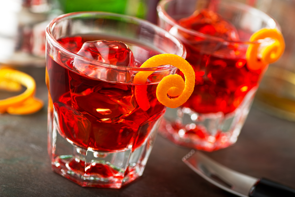 Two glasses of red negronis with orange peels.