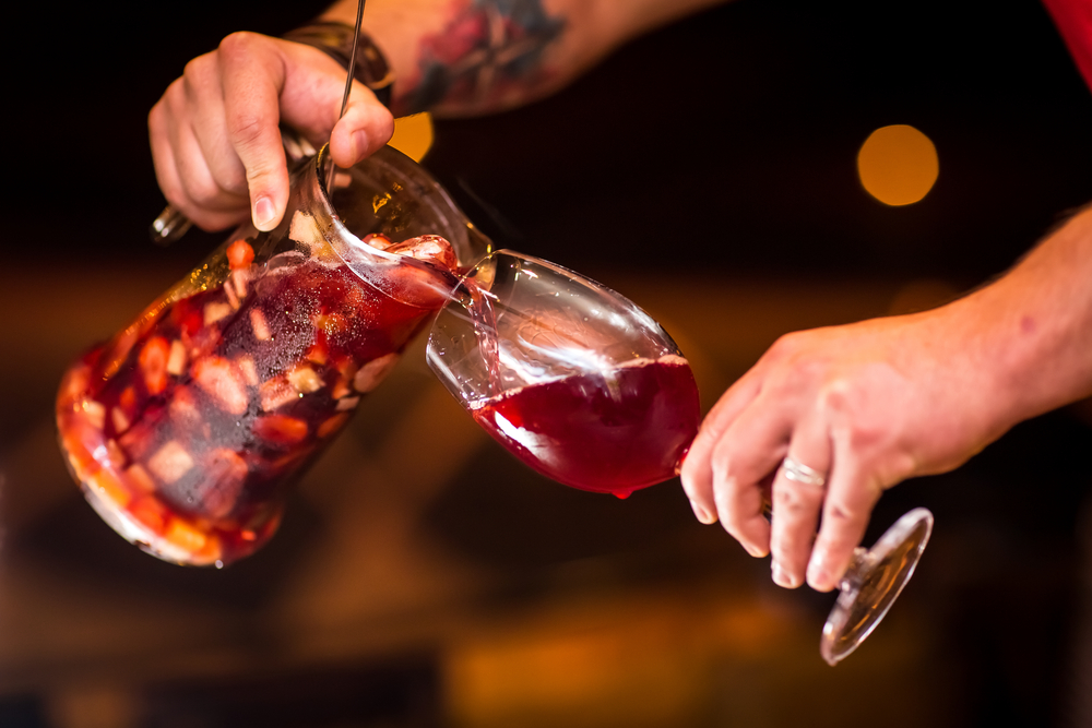 A person pouring a pitcher of sangria into a wine glass.