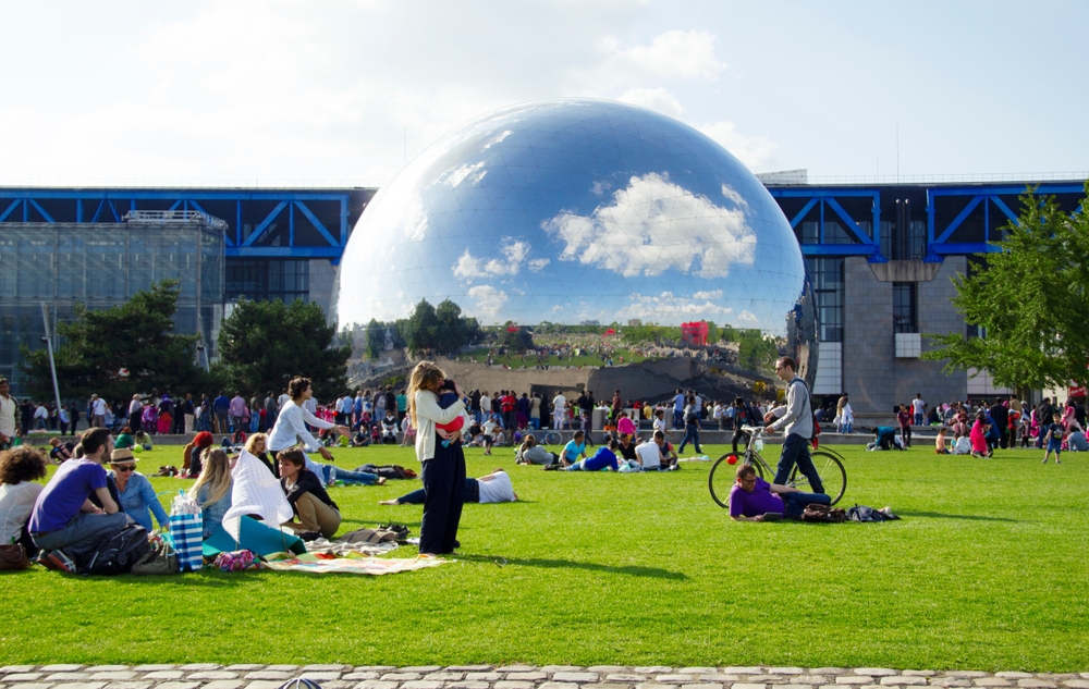 People lounging in a park with a big metal ball in the background.