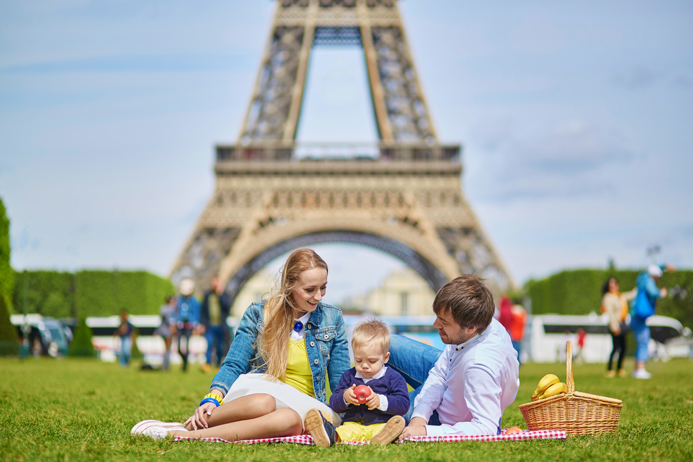 A family with a toddler enjoys a picnic under the Eiffel Tower on a sunny day in Paris.