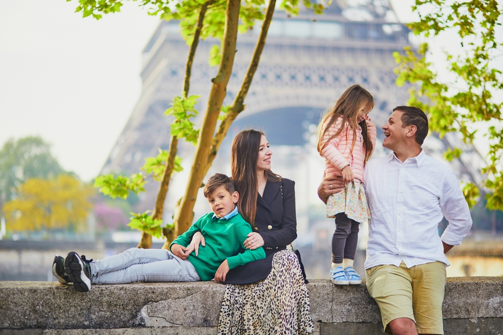 A family of four sits on a wall with the Eiffel Tower in the background.