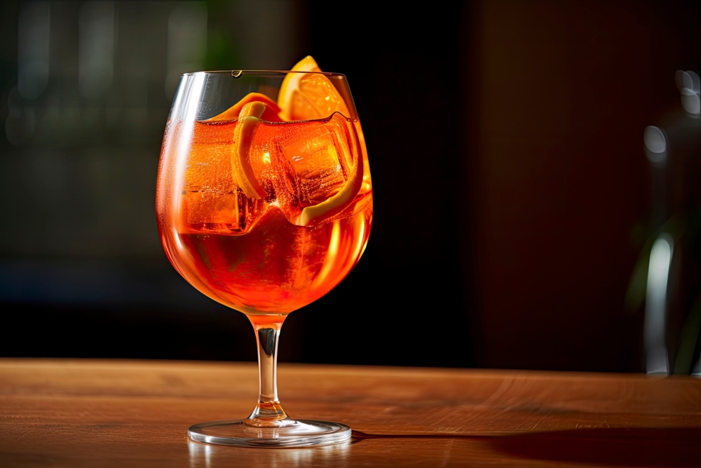 Glass of Aperol Spritz with ice cubes and an orange on a bar top.