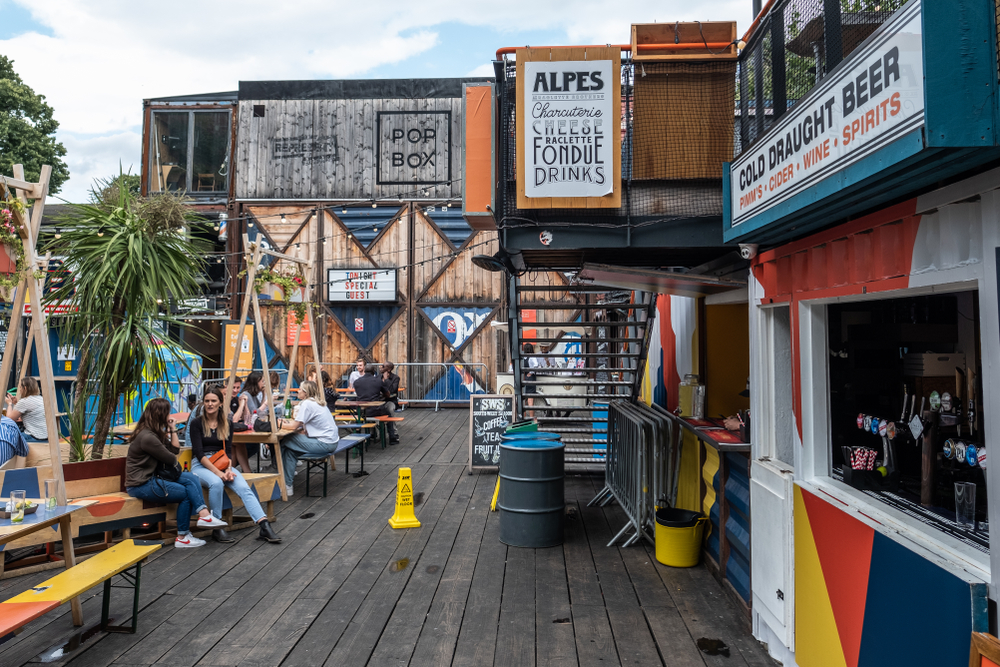 a street food, bar and nightlife location made from reused shipping containers in Brixton, south west London. The people shows people sat at tables. 