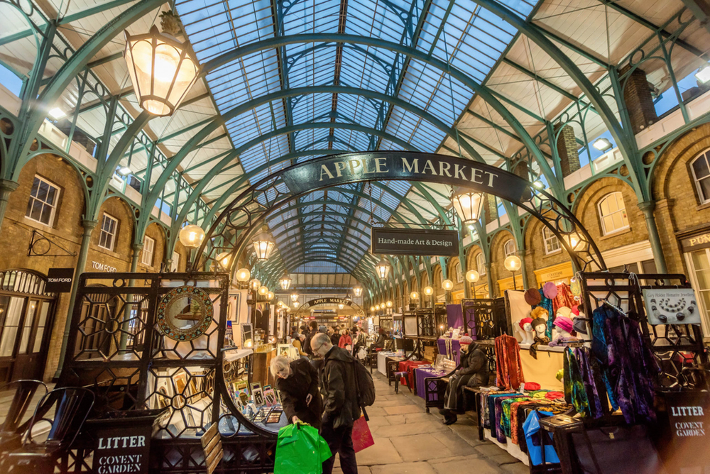 Market stalls under glass buildings with people selling food and clothes. Best markets in London