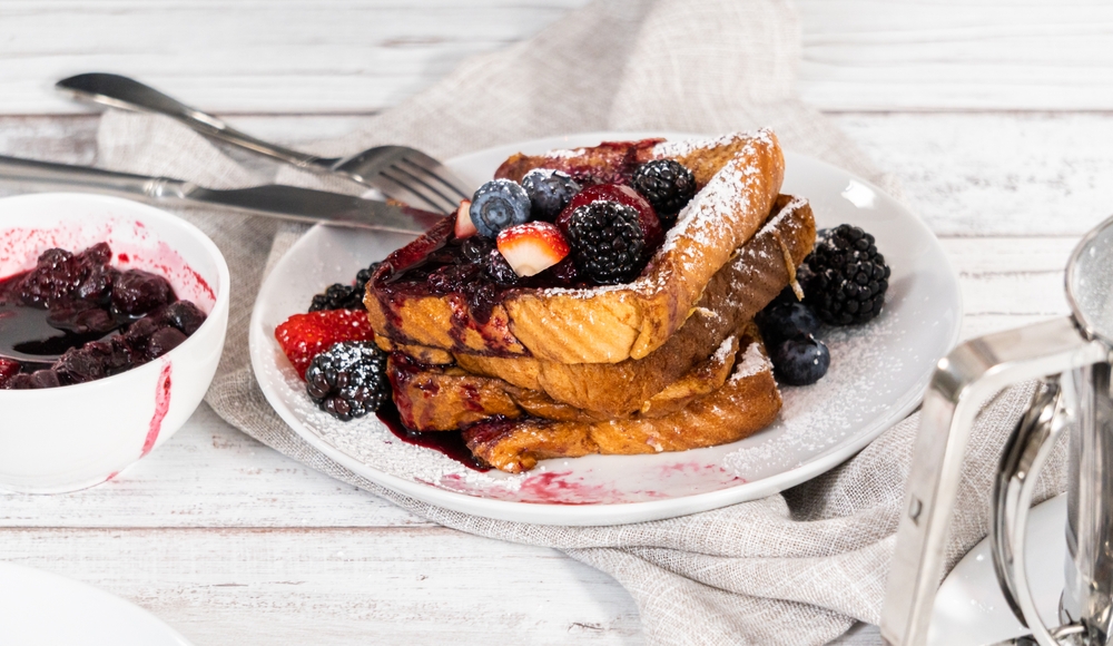 Stack of freshly made french toast garnished with mix berry compote and powder sugar