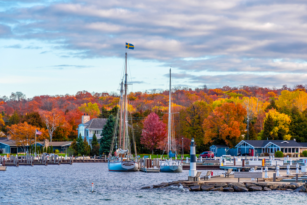 sailboats in harbor with brightly colored trees and cloudy sky in background