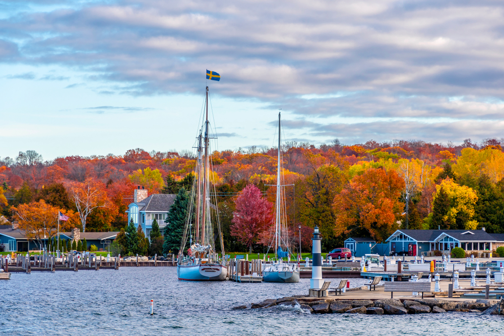 Brightly colored leaves in background with sailboats moored in blue water in foreground at romantic getaways in the Midwest