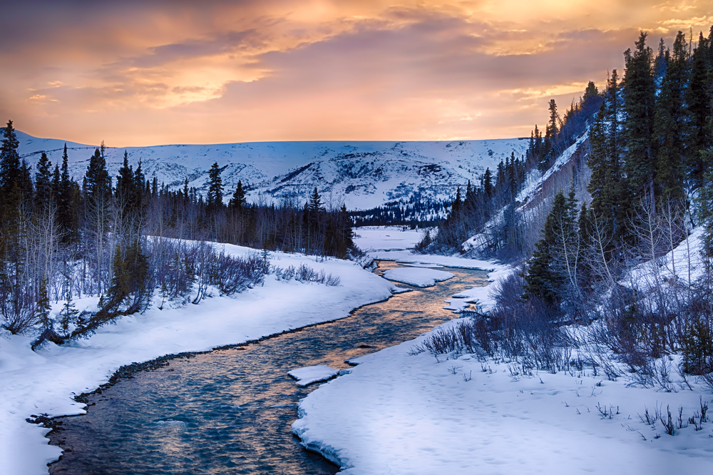 Pink sunset over a snowy river and mountains in Alaska in winter.