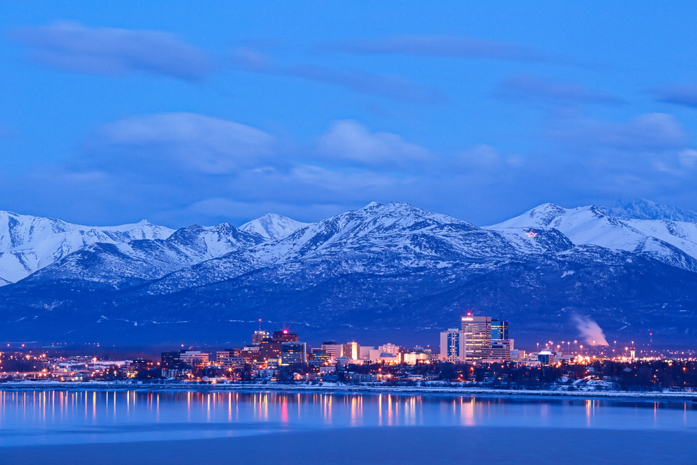 Blue dusk over the city lights of Anchorage with snowy mountains in the background.