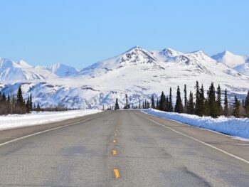 Plowed highway heading towards mountains in Alaska in winter.