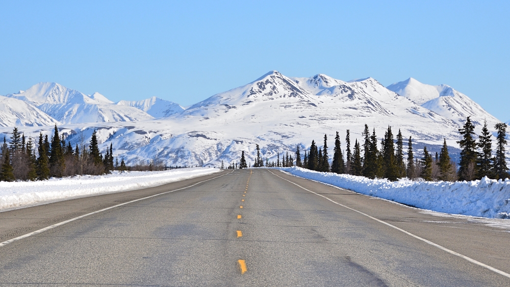 Paved highway on a snowy day heading towards mountains in Alaska.