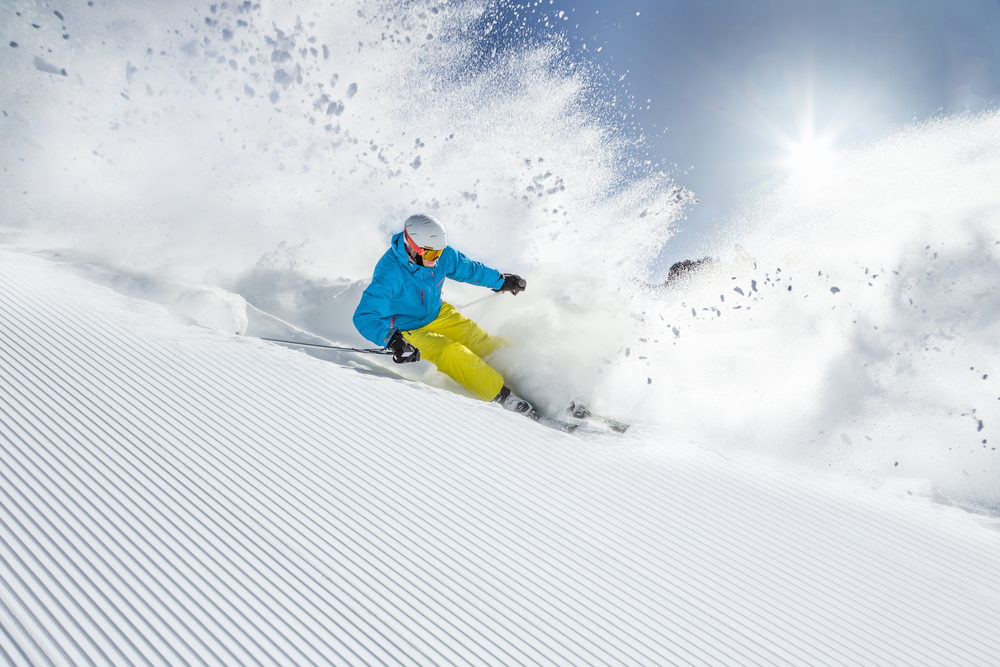 Skier in bright colors going down fresh snow with powder spraying everywhere.