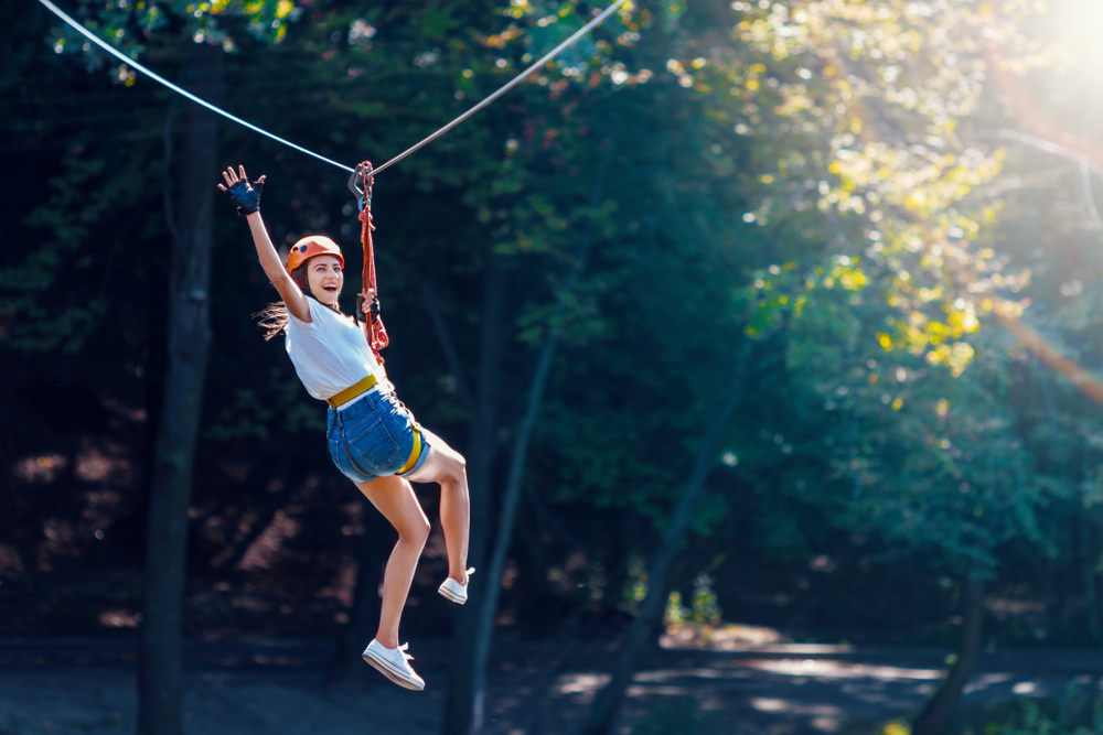 A young woman ziplining in the woods on a sunny day