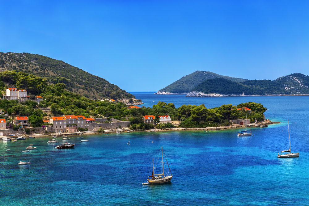 Aerial view of the island of Kolocep with bright blue water and boats.