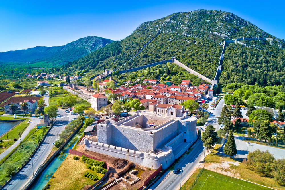 Town of Ston with a fortress and stone walls going up a green hill.