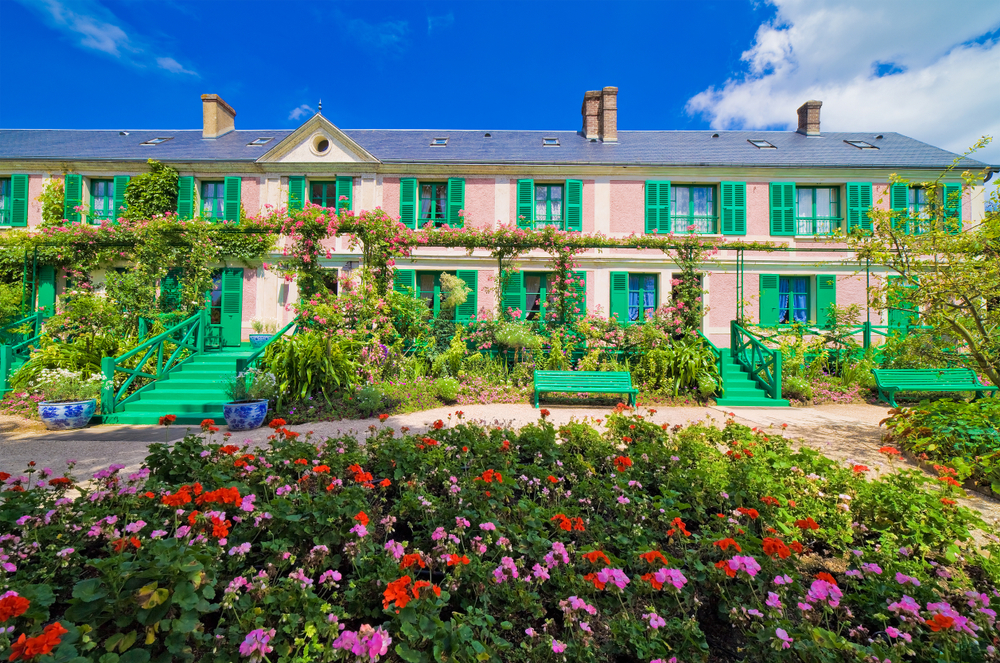 Claude Monet House, Giverny. The house is pink and green and has lots of flowers around it. 