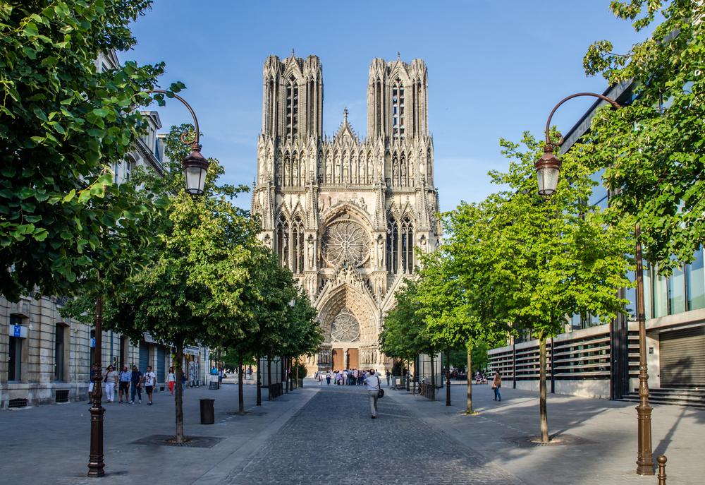 View of the facade of the cathedrale of reims taken from down a street with trees either side.  